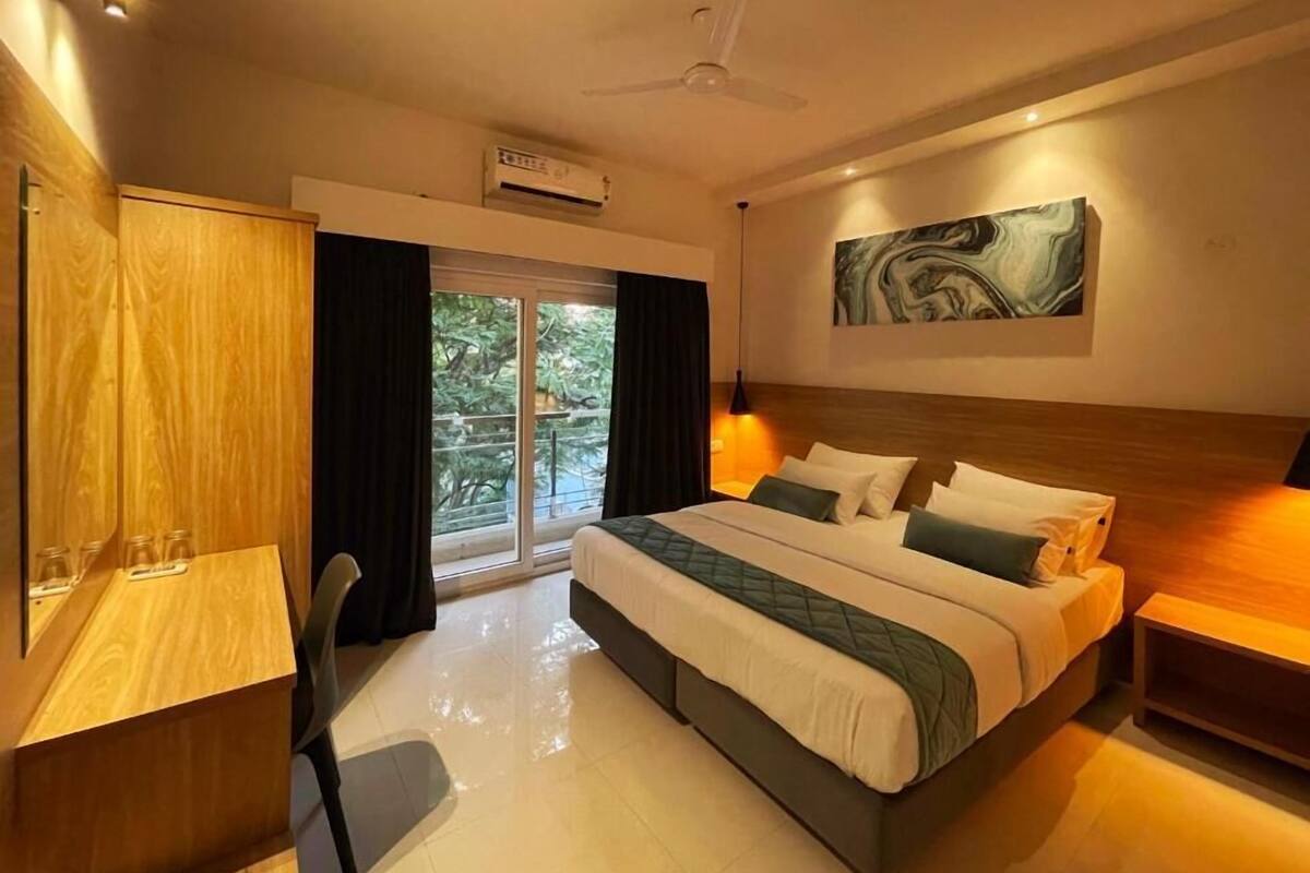 A hotel room with a large bed, a desk, a chair, a nightstand, a ceiling fan, and a window with curtains.