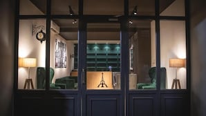 Una habitación con un ventanal grande, un sillón verde, una lámpara y una estantería.