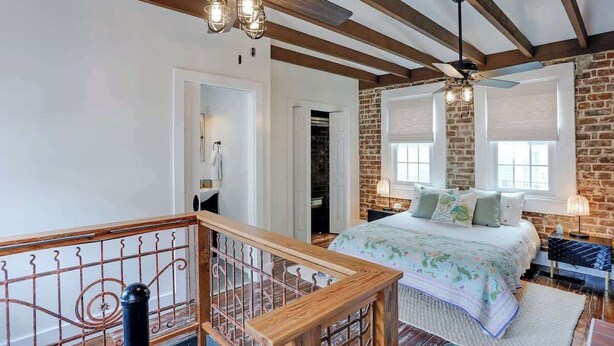 A bedroom with a bed, a wooden ceiling, a brick wall, and a window. - Cozy Historic 1790 Guest House Steps to River St (Savannah)