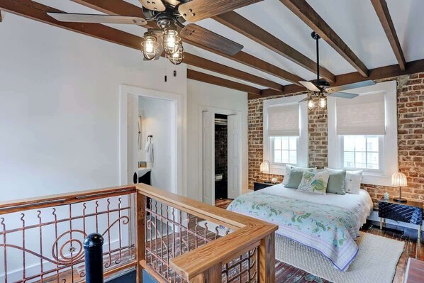 A bedroom with a bed, a wooden ceiling, a brick wall, and a window.