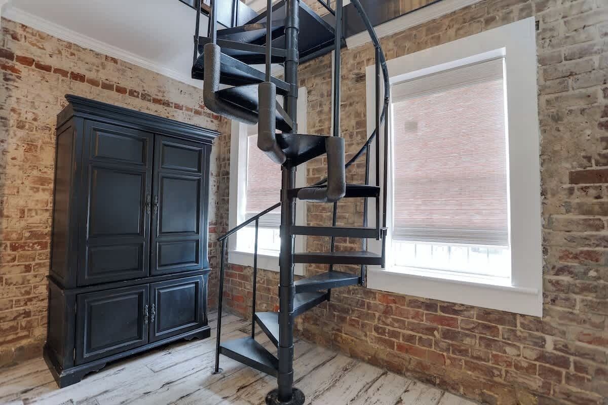 A spiral staircase in a room with exposed brick walls and a large window.
