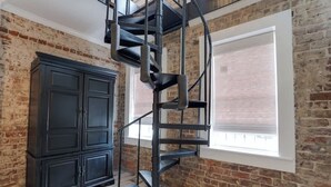 A spiral staircase in a room with exposed brick walls and a large window. - Cozy Historic 1790 Guest House Steps to River St (Savannah)