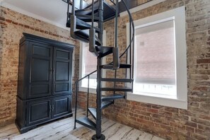 A spiral staircase in a room with exposed brick walls and a large window.