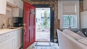 A kitchen with white cabinets, a red door, and a view of the outside. - Cozy Historic 1790 Guest House Steps to River St (Savannah)