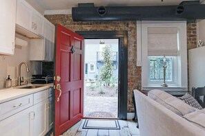 A kitchen with white cabinets, a red door, and a view of the outside.