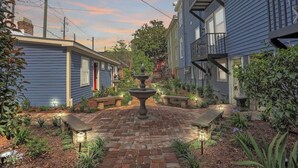 A courtyard with a central fountain, surrounded by brick pathways and small plants. - Cozy Historic 1790 Guest House Steps to River St (Savannah)