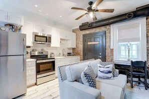 A modern kitchen with white cabinets, stainless steel appliances, and a brick accent wall.