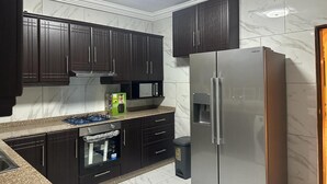 A modern kitchen with dark cabinets, a stainless steel refrigerator, and a built-in oven. - 3 Bed Apartment Sleeps 6 - Ensuites, Parking, Wifi (Freetown)