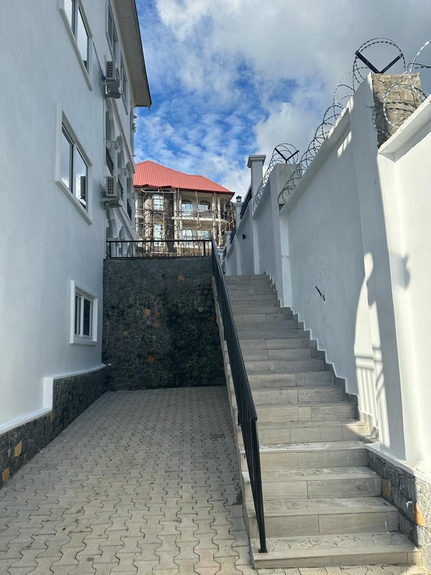 A staircase leading to a building with a red roof, surrounded by white walls and a stone base.