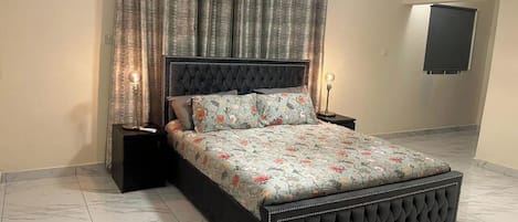 A bedroom with a tufted headboard, floral bedding, and a large mirror on the wall.