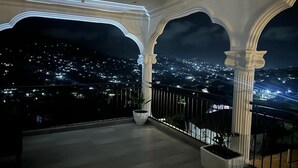 A balcony with white columns and a view of a city at night.