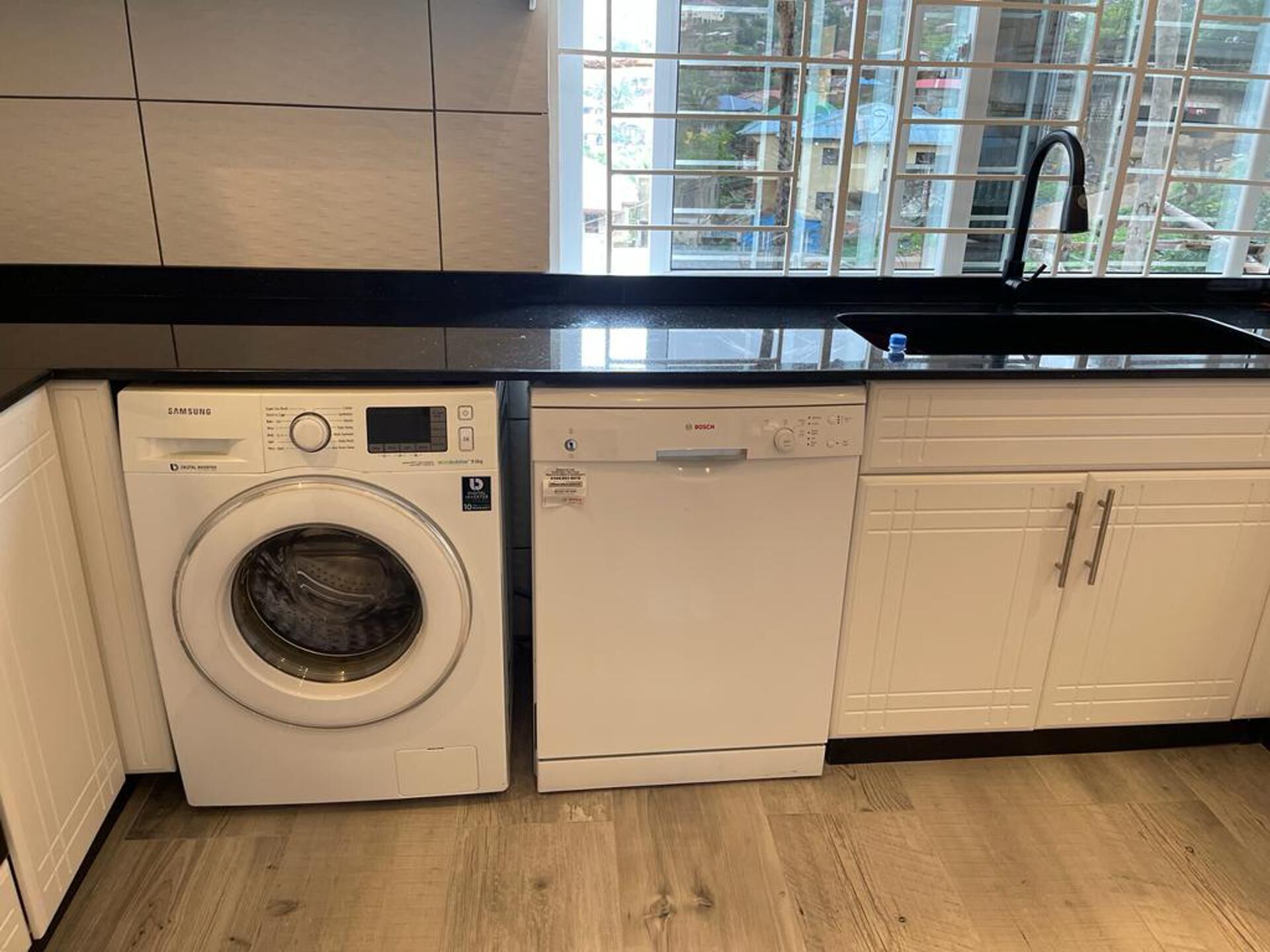 A compact kitchen with a washing machine, dishwasher, and a window with a view of buildings.
