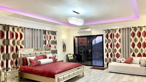 A bedroom with a large bed, a sofa, a chandelier, and curtains with a geometric pattern.