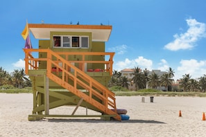 Une tour de surveillance avec un escalier en bois, un drapeau et des chaises pour les sauveteurs, sur une plage de sable.