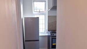 A narrow hallway leading to a kitchen with a refrigerator, stove, and window.