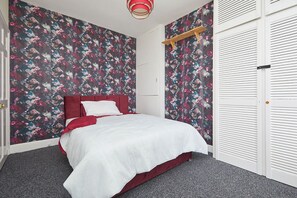 A bedroom with a bed, a wardrobe, and a floral-patterned wall. - Comfortable 4-bed House in Hucknall, Nottingham (Nottingham)