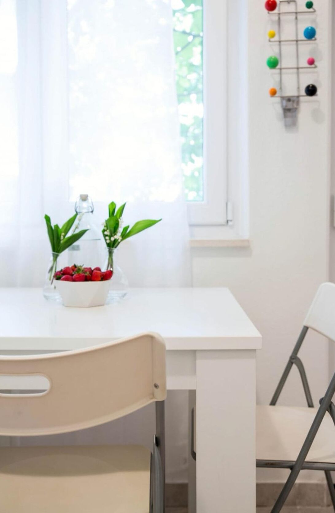 A white table with a bowl of strawberries and two potted plants.