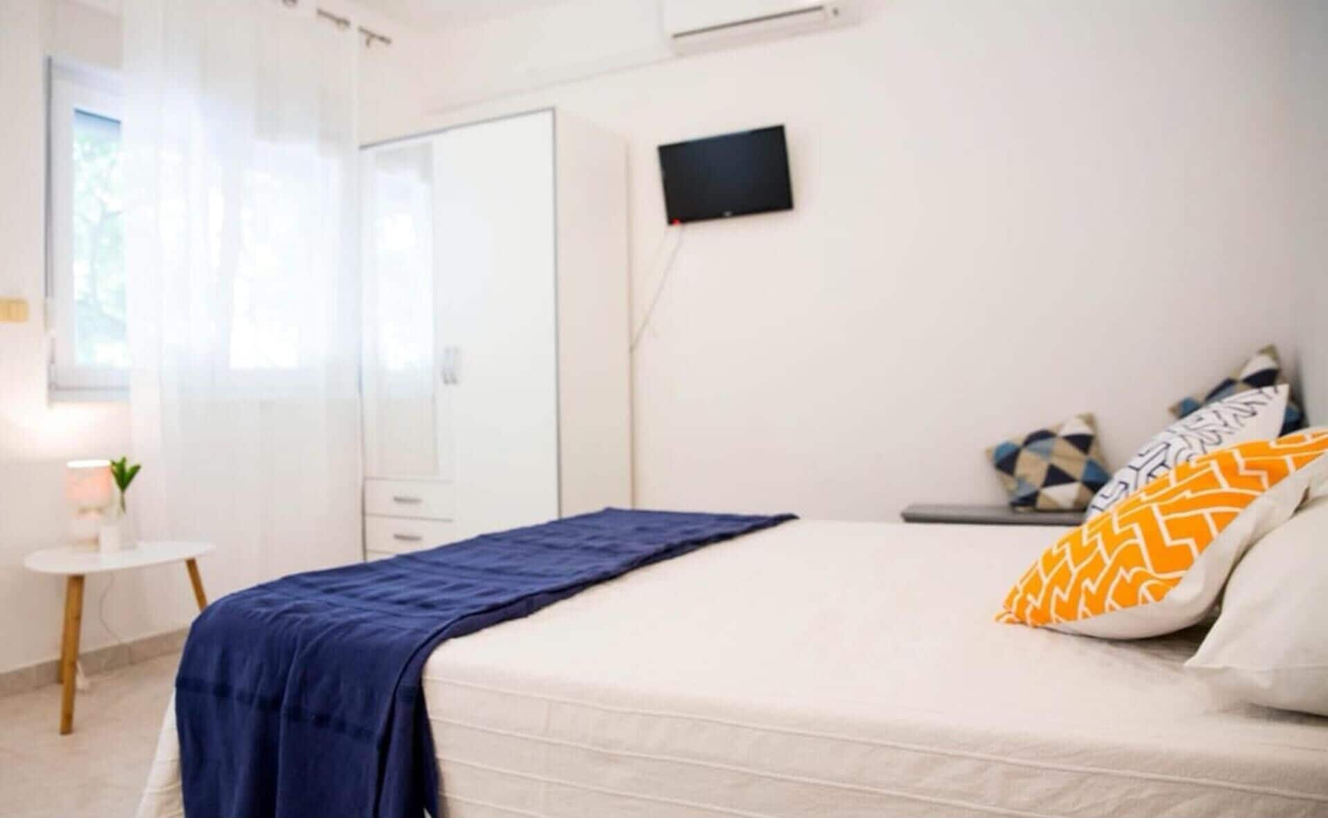 A bedroom with a bed, a TV, a bedside table, and a window.