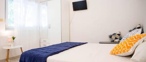 A bedroom with a bed, a TV, a bedside table, and a window.