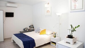 Un dormitorio con cama, mesitas de noche, televisor, lámpara y planta.