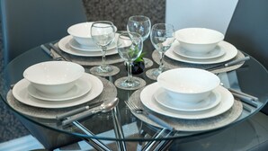Une table ronde en verre, mise pour quatre personnes, avec des assiettes blanches, des bols et des verres à vin transparents.