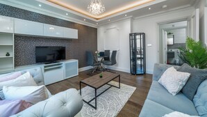 Un salon moderne avec un téléviseur à écran plat, un canapé, une table basse et un lustre.