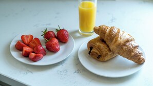 Une table mise pour le petit-déjeuner avec une assiette de fraises, un verre de jus d’orange et un croissant posés sur un plan de travail en marbre.