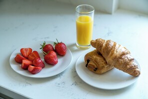 A breakfast setting with a plate of strawberries, a glass of orange juice, and a croissant on a marble countertop. - Madika Homes Luxe Apartment in Mill Hill (London)