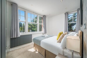 A bedroom with a bed, bedside table, and a window with curtains. - Madika Homes Luxe Apartment in Mill Hill (London)