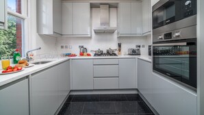 Une cuisine moderne avec des meubles blancs, un sol carrelé noir et des appareils électroménagers en acier inoxydable.