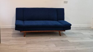 Un canapé bleu foncé, doté de pieds en bois, se trouve dans une pièce dont le sol est recouvert de parquet clair et les murs sont peints en blanc.