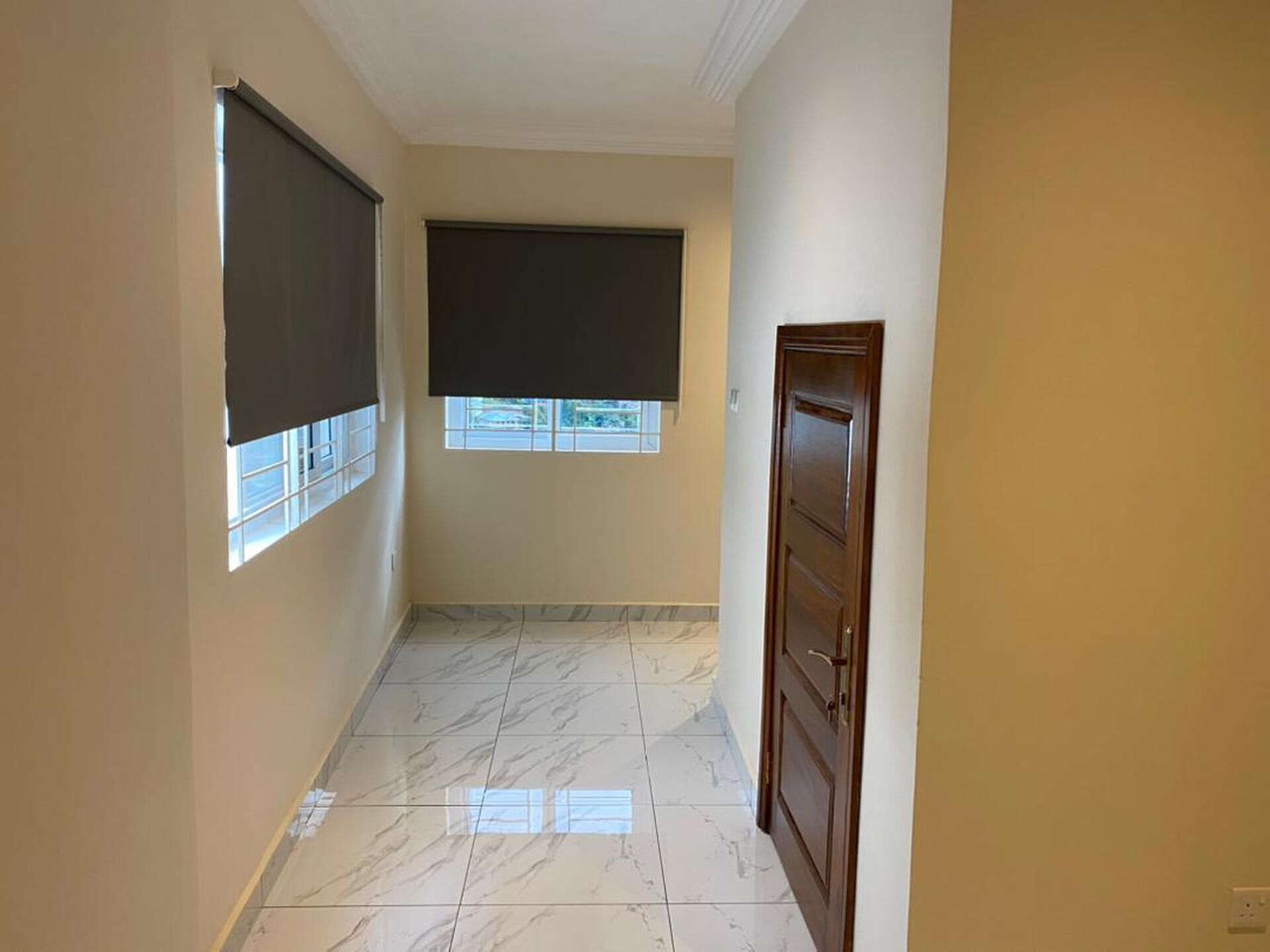 A hallway with a marble floor, a door on the right, and two windows with blinds.
