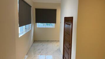 A hallway with a marble floor, a door on the right, and two windows with blinds.