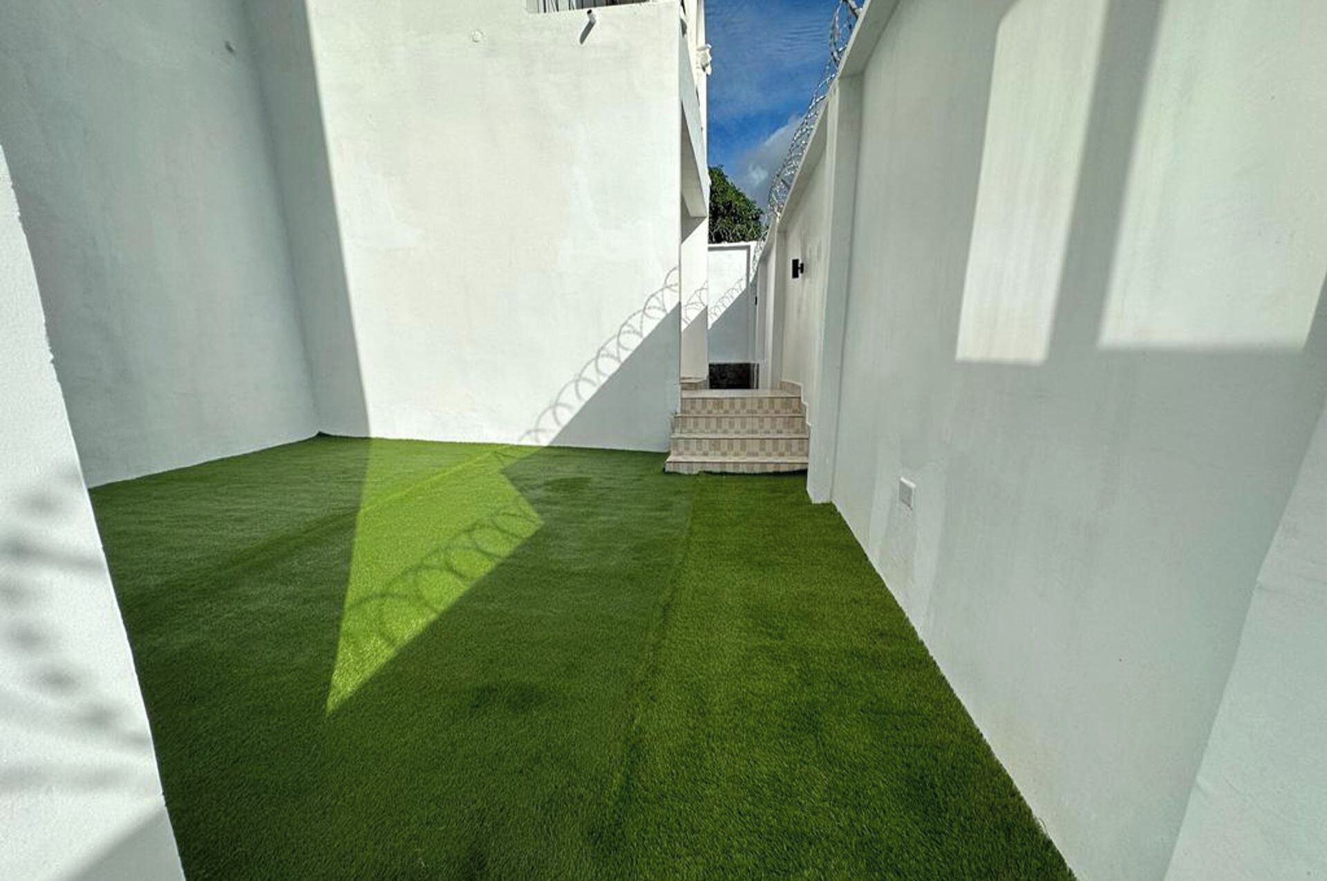 Un pasillo estrecho con paredes blancas y suelo de césped artificial, que conduce a una escalera.