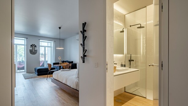 Een moderne slaapkamer met een groot bed, een bureau en een stoel, een badkamer met een glazen douche, en uitzicht op de omgeving.