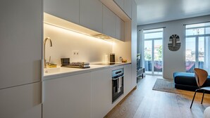 Een moderne keuken met een ingebouwde oven en magnetron, een zithoek met een donkere bank en een houten stoel, en grote ramen met uitzicht op het omliggende landschap.