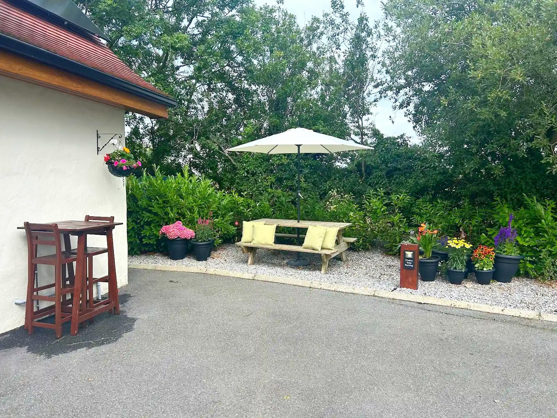 Een terras met een houten tafel en stoelen, een bankje en een hangende bloempot.