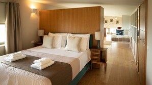 A hotel room with a large bed, wooden headboard, two bedside tables with lamps, a wooden floor, and a view of the hallway. - Villa - Sleeps 10 - Pool - Parking - Pool Table (Heraklion)
