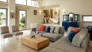 A spacious living room with a grey sofa, patterned armchairs, a wooden coffee table, and a chandelier. - Villa - Sleeps 10 - Pool - Parking - Pool Table (Heraklion)