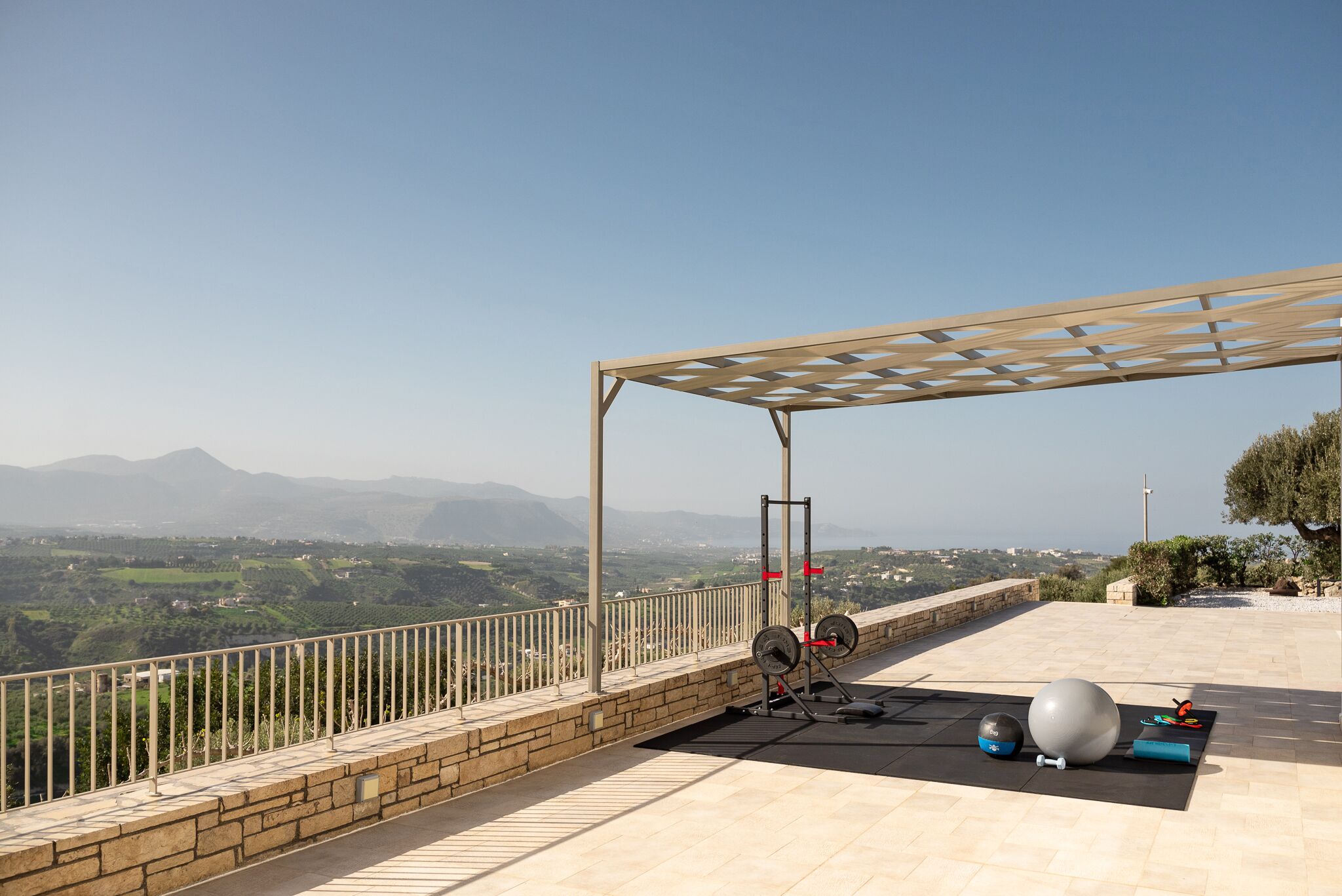 Ein Trainingsbereich im Freien mit Blick auf Berge, einer Pergola und Fitnessgeräten.