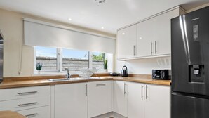 Een moderne keuken met witte kasten, een roestvrijstalen koelkast en een raam met uitzicht op het dak.