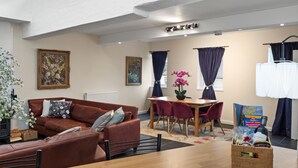 Een moderne woonkamer met een bruine leren bank, een houten eettafel en een klein keukentje.