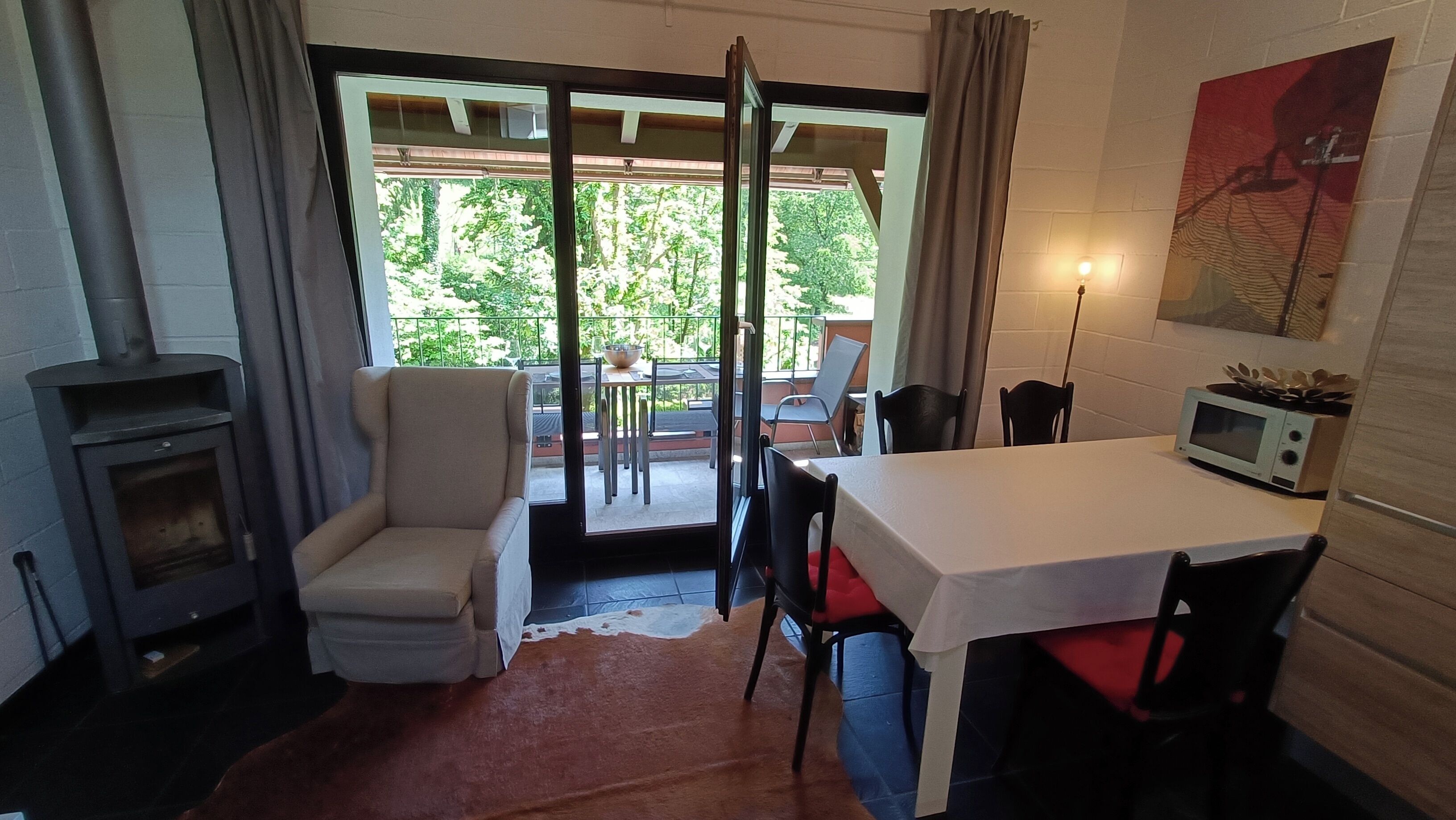 Une pièce chaleureuse avec une cheminée, une table à manger et des chaises. Une porte-fenêtre coulissante donne accès à un espace extérieur aménagé avec une table et des chaises.
