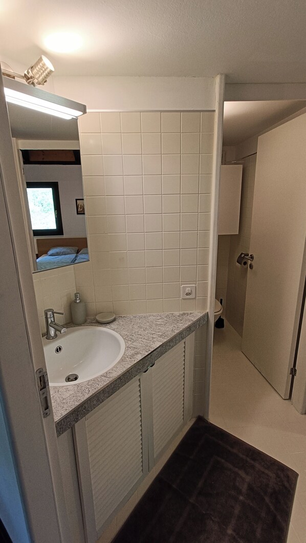 Une salle de bain avec un lavabo blanc, un miroir et un mur recouvert de carreaux.