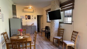 A dining area with a wooden table and chairs, a kitchen in the background, and a TV mounted on a pillar.