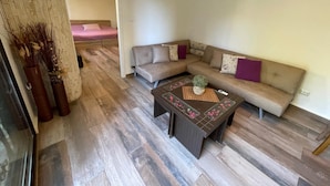 A living room with a sectional sofa, a coffee table, and a bed in the background.