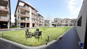 A courtyard with a lawn, outdoor seating, and a building with multiple balconies.
