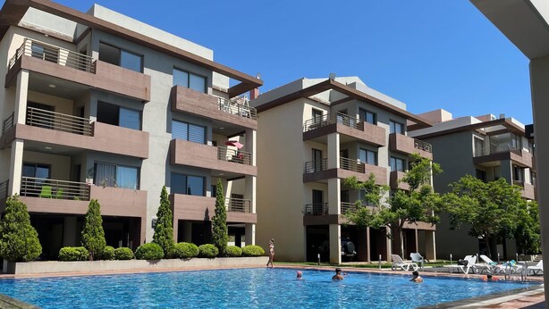 A modern multi-story residential building with balconies, a swimming pool, and a landscaped garden.