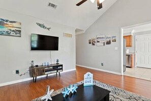 A living room with a flat-screen TV, wooden flooring, and a ceiling fan.
