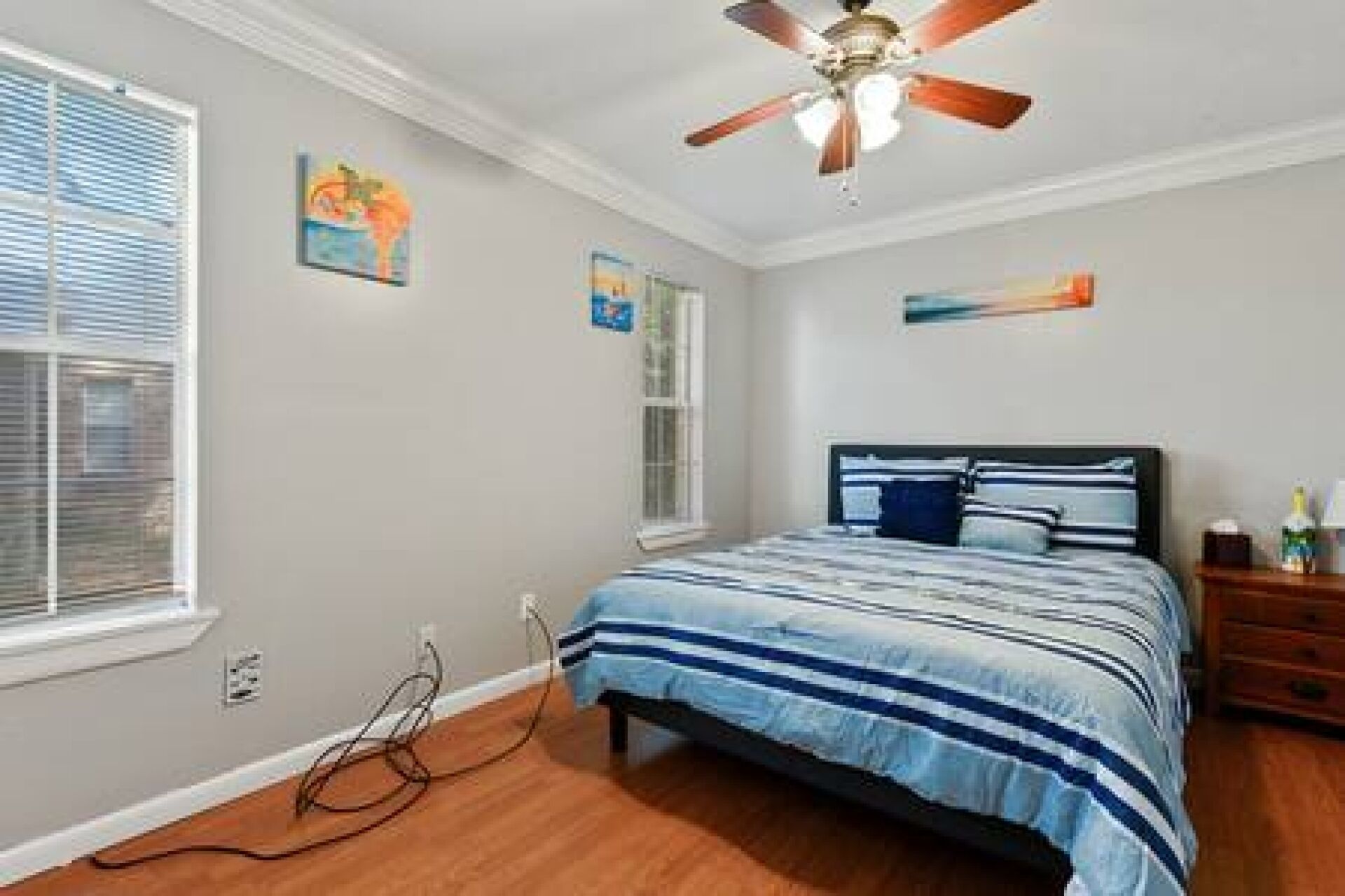 A bedroom with a bed, a ceiling fan, a window, and artwork on the walls.